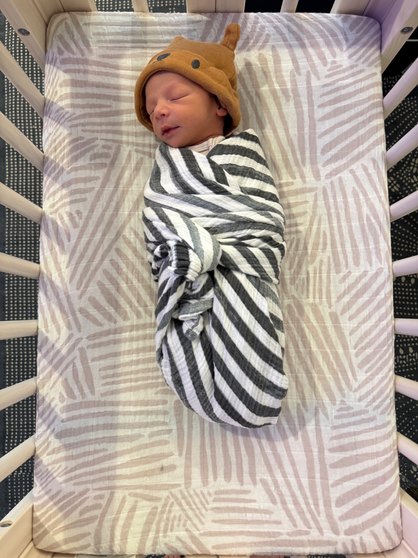 Ollie swaddled in stripes with an acorn hat in the crib